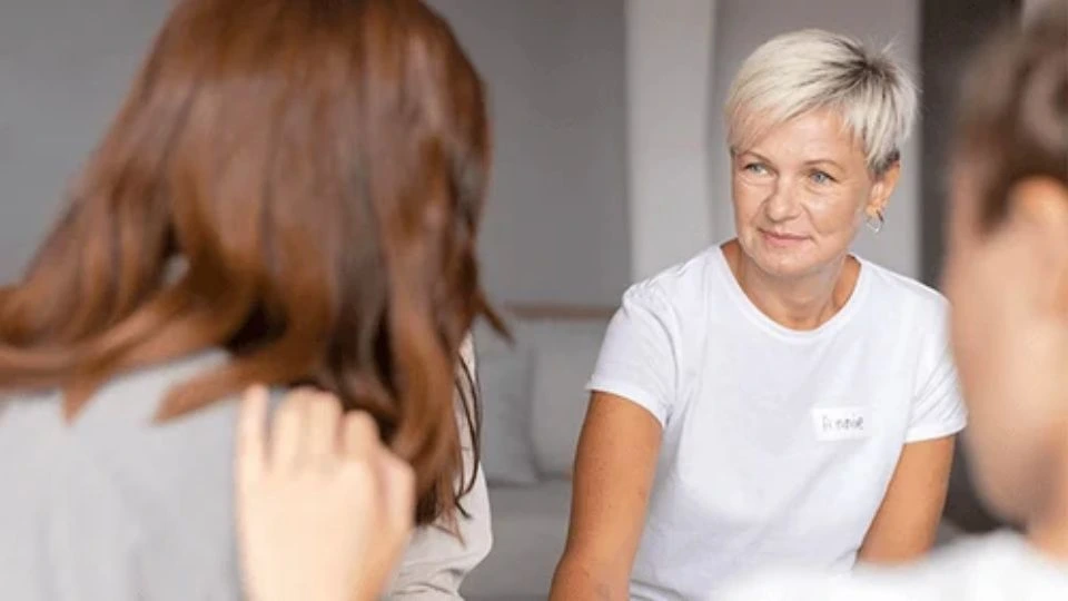 Une femme aux cheveux courts échange attentivement avec deux personnes dans un cadre convivial.