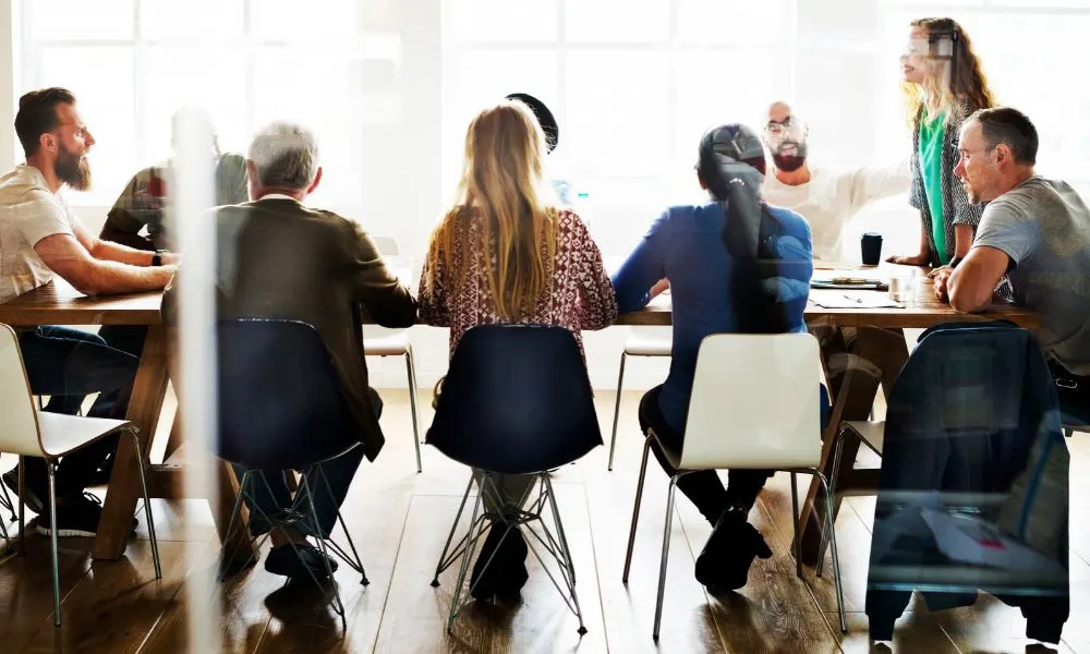 Un groupe de personnes participe à une réunion autour d’une grande table dans une salle lumineuse.