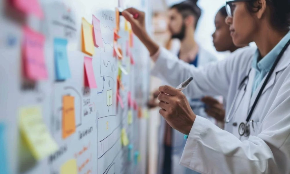 Des professionnels de santé dessinent un schéma de processus avec des flèches et des post-it sur un tableau.