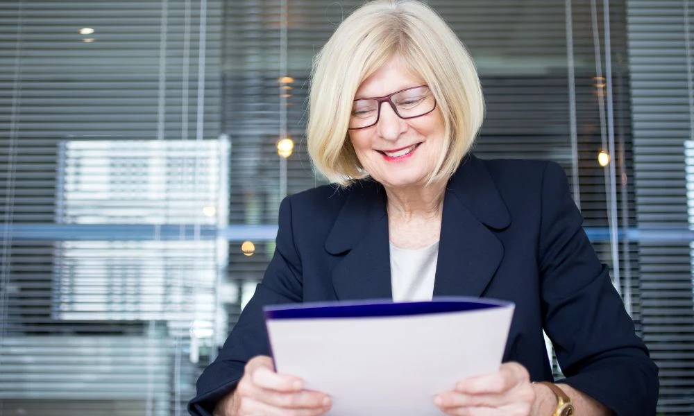 Femme souriante assise à un bureau tenant un dossier.
