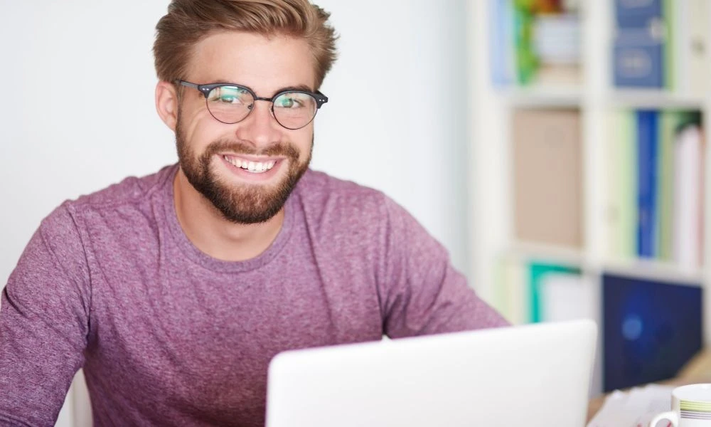 Un homme souriant travaille sur un ordinateur dans un bureau lumineux.