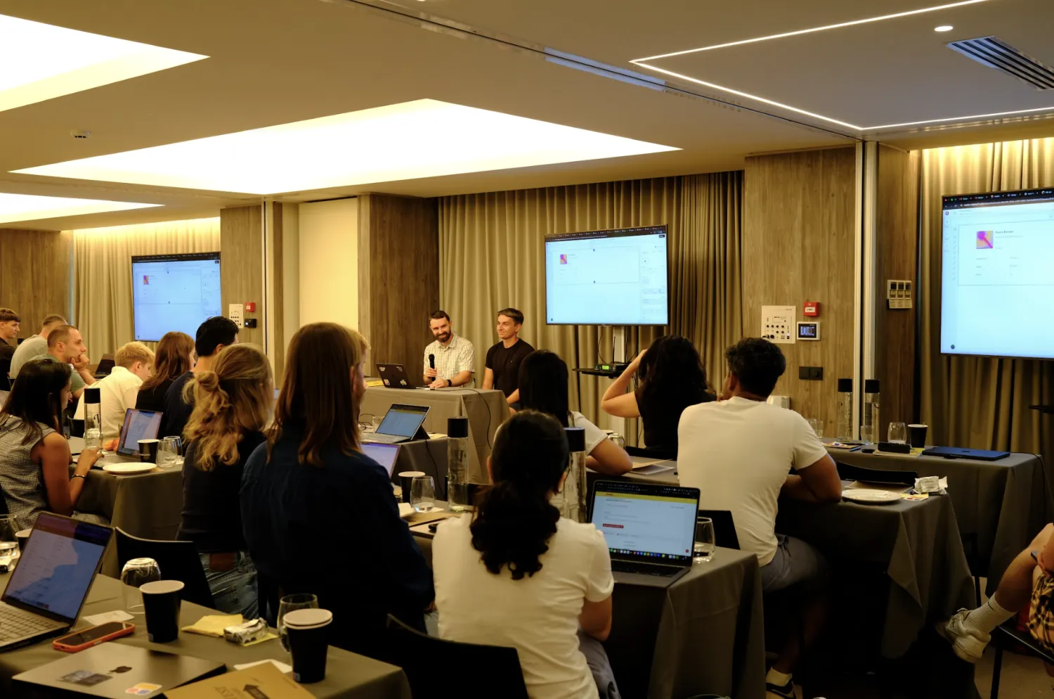 Softr team with laptops watching two teammates present on screens in a conference room