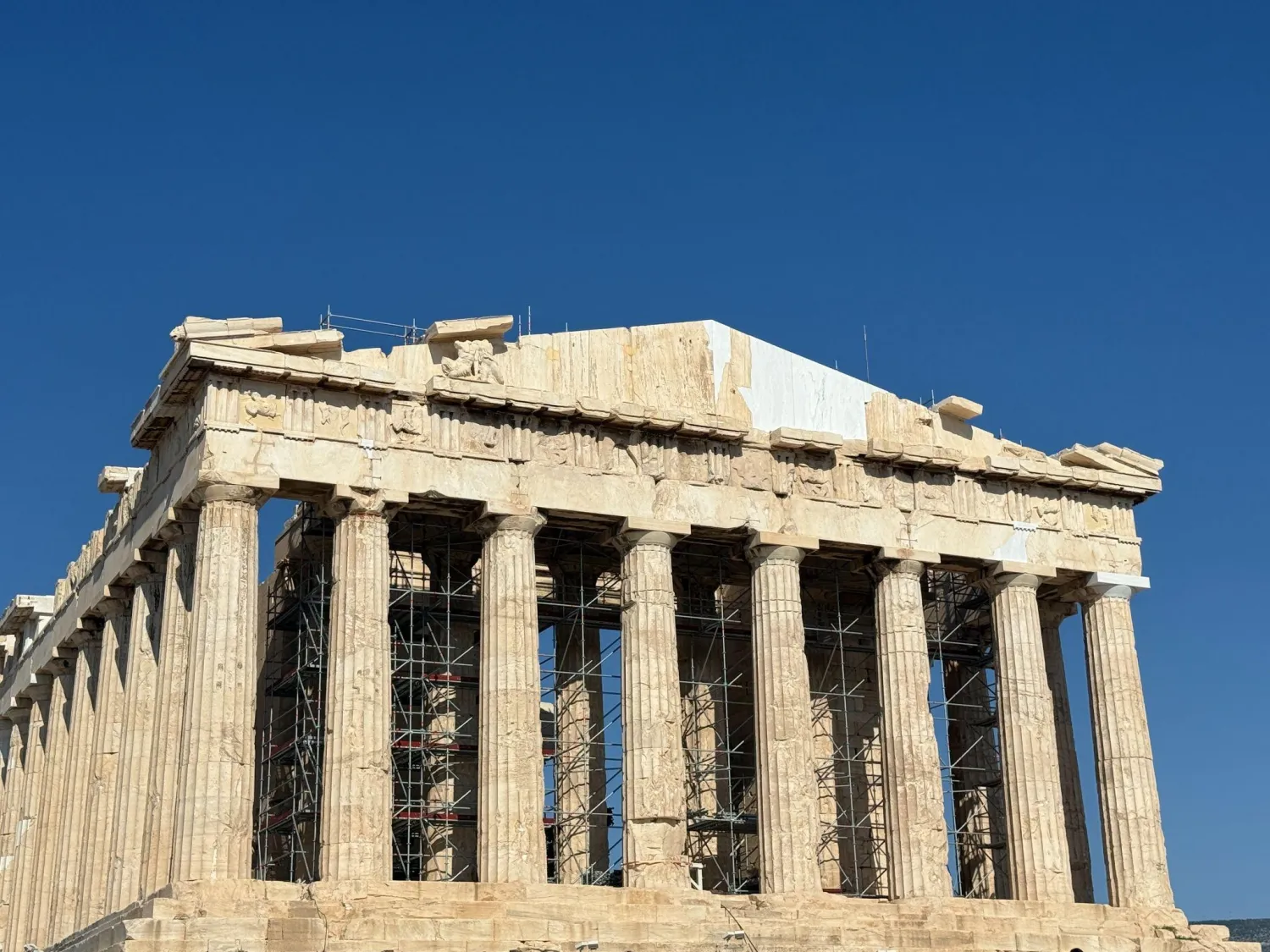 The Parthenon on the Acropolis under a clear blue sky, with scaffolding between its columns