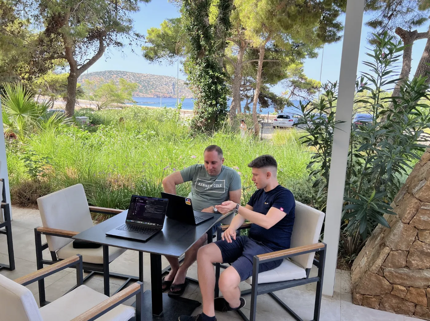 Two Softr engineers working on laptops at an outdoor table overlooking the sea