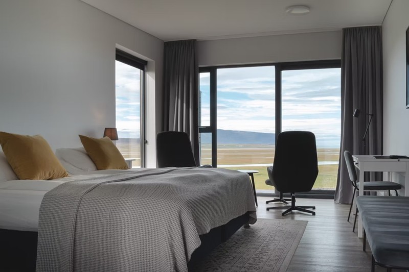 Guest room at Hofsstaðir Country Hotel with a double bed, two armchairs and large windows over open farmland toward distant mountains