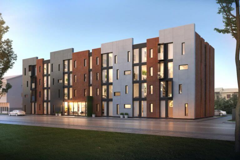 Hotel South Coast, a four-storey building with brown and grey panel facades and large lit windows, seen from the street at dusk
