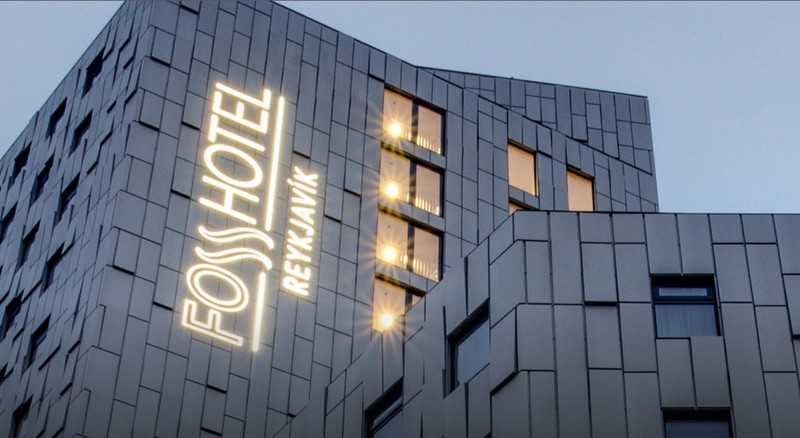 Fosshótel Reykjavík, a grey angular building with an illuminated hotel sign and warmly lit windows at dusk