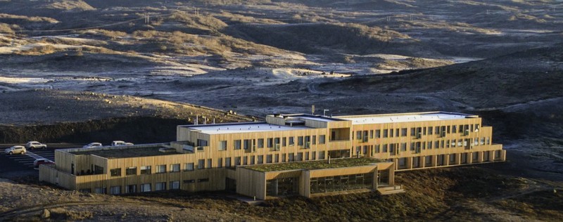 Fosshótel Mývatn, a long timber-clad hotel with turf-covered sections sitting on a barren lava landscape in low sun