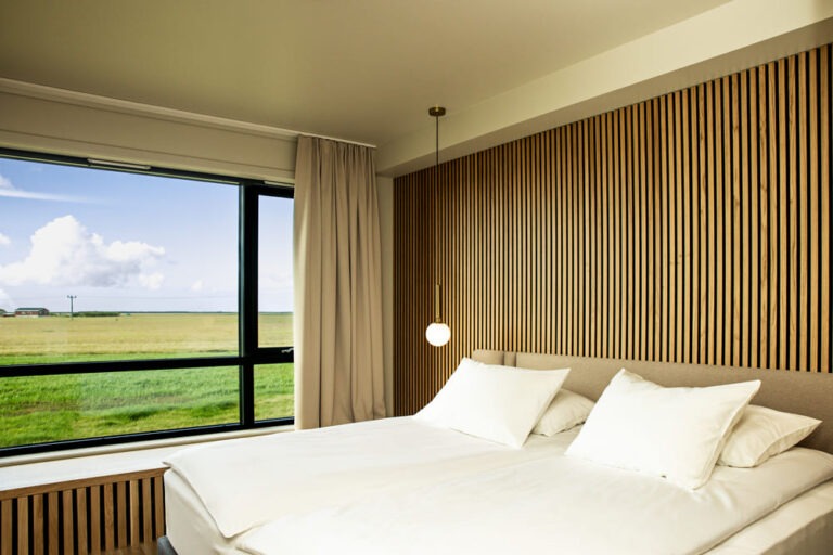 Guest room at Hotel Lóa with a double bed, a slatted oak feature wall and a large window overlooking green farmland