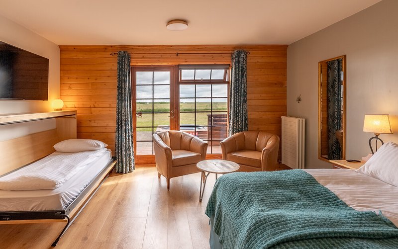 Guest room at Hotel Rangá with pine-paneled walls, a double bed and fold-down single bed, two leather armchairs and glass doors opening to a terrace and open fields