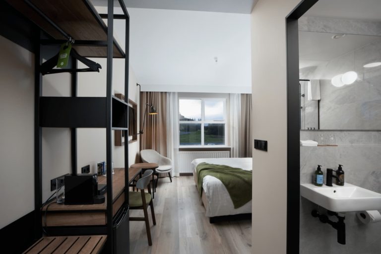 Deluxe room at Hótel Klaustur with a double bed under a green throw, a desk and open wardrobe, and a marble bathroom visible through the doorway