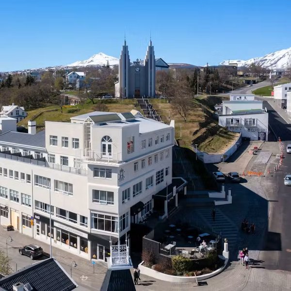 Aerial view of Hótel KEA, a white multi-story hotel in central Akureyri, with the twin-spired Akureyrarkirkja church and snow-capped mountains behind