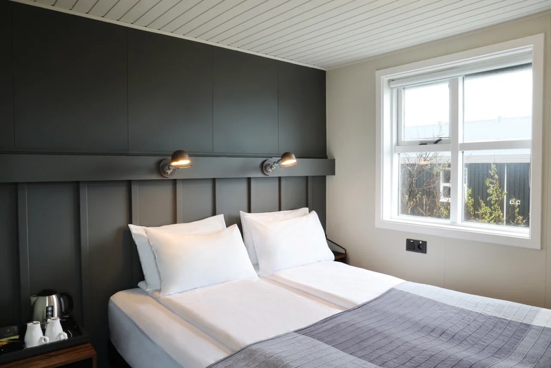Guest room at Fosshotel Hellnar with a double bed, dark gray paneled headboard wall with two reading lamps and a window with white frames