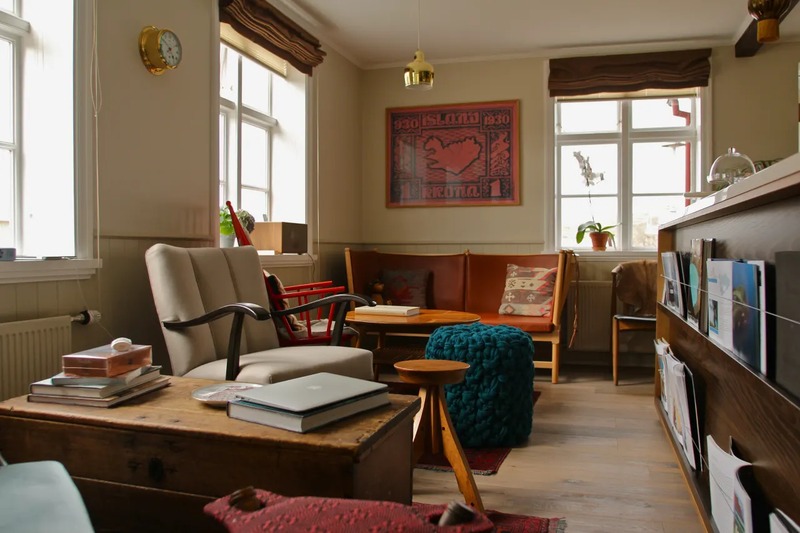 Cozy lounge at Hotel Egilsen with vintage armchairs, a leather bench, a wooden coffee table, a teal knitted pouf and a framed Icelandic stamp poster on the wall