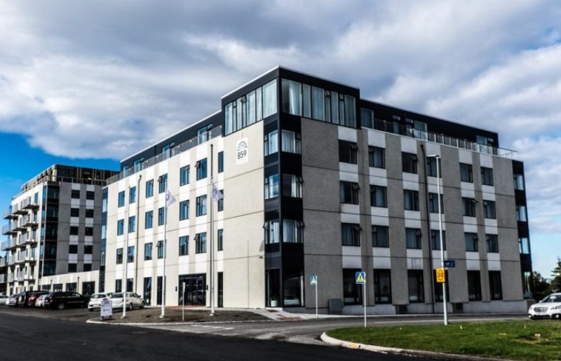 Exterior of Hótel Vesturland in Borgarnes, a modern five-story gray and white building with dark window bands under a cloudy blue sky