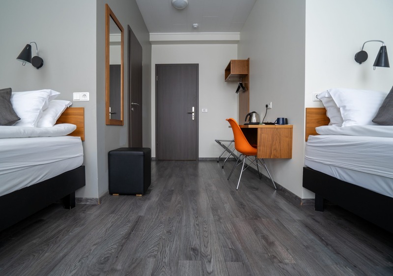 Twin room at Hotel Valaskjálf with two white-linen beds, wood headboards, black wall lamps, a wall-mounted desk with an orange chair, and dark gray wood flooring