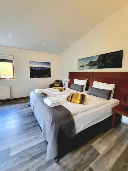 Guest room at Hotel Flókalundur with a double bed, mahogany headboard, gray throw and yellow striped pillows, and coastal cliff photographs on the walls