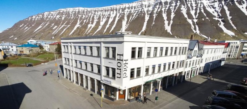Exterior of Hótel Horn in Ísafjörður, a white corner building with the hotel name on its facade, below a steep snow-streaked mountain
