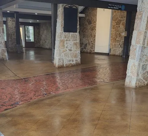 Indoor space with stone pillars and walls, featuring a curved reddish brick-patterned floor section amidst brown tiled flooring.