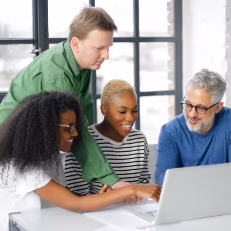 four people looking at a laptop in an office