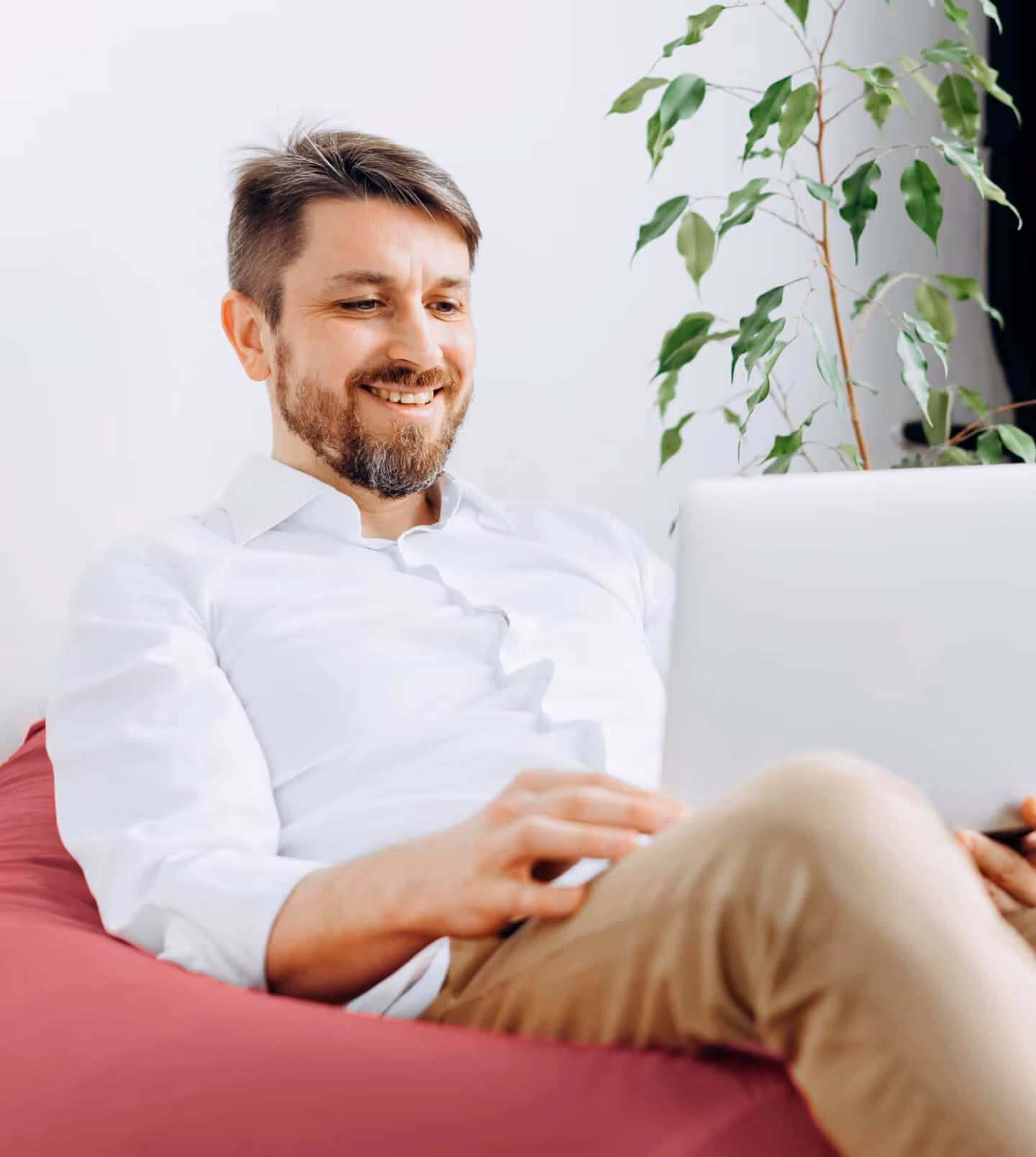 Middled man, sat on a colorfull bean bag, looking into his laptop screen and smiling