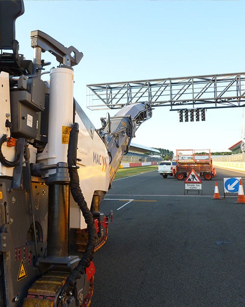 Road planer milling a carriageway beside an overhead gantry
