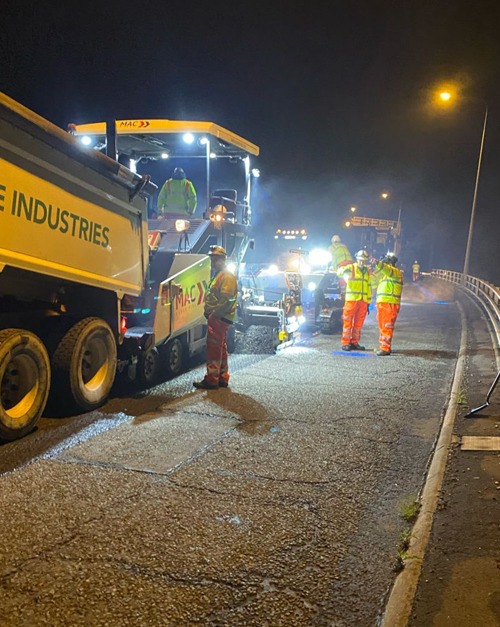 Surfacing crew carrying out highway maintenance at night under lighting