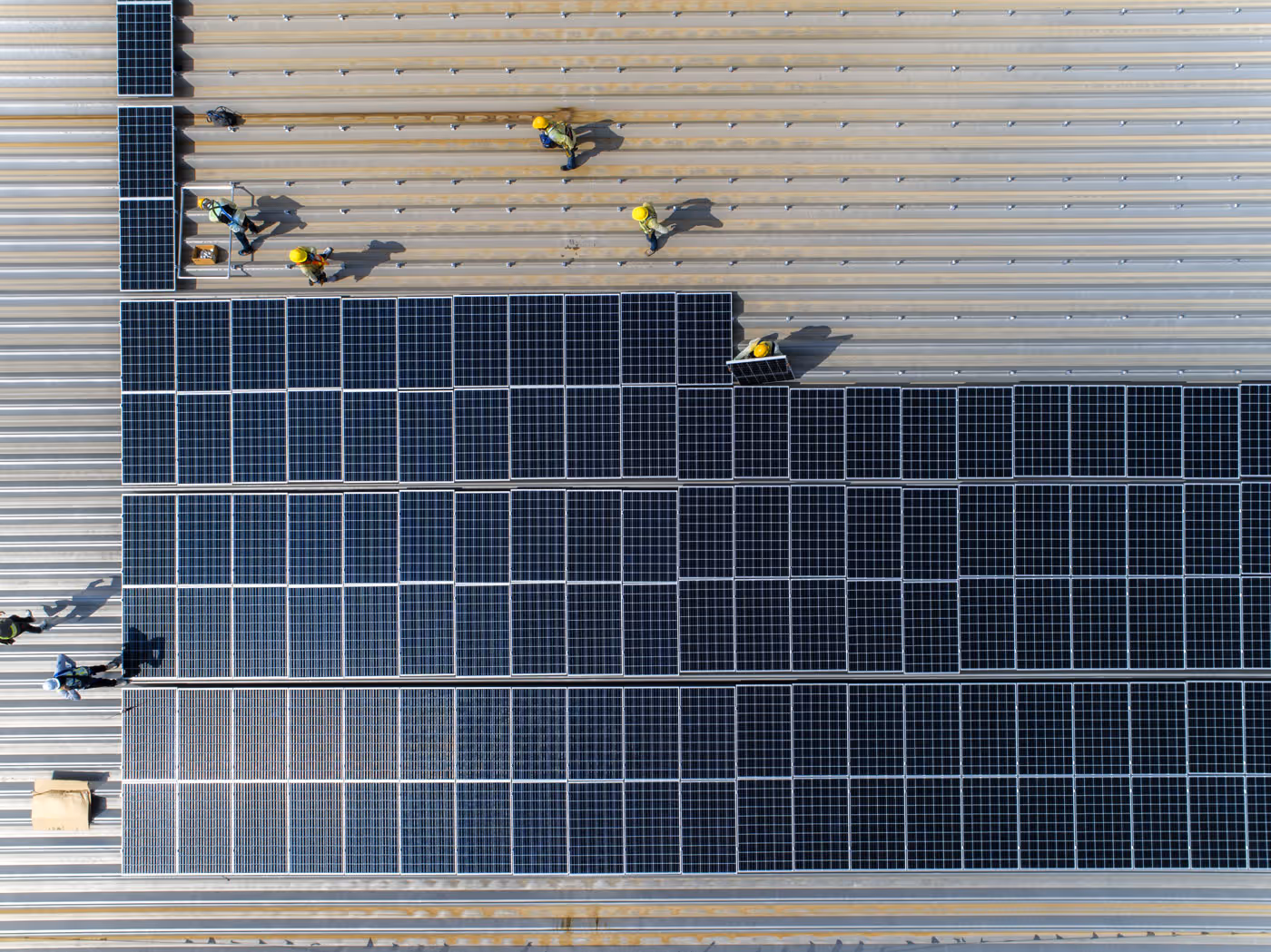 Aerial shot of workers installing solar panels on industrial roof
