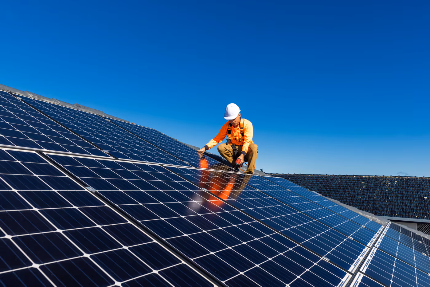 Man installing solar panel on roof in orange hi-vis and white helmet