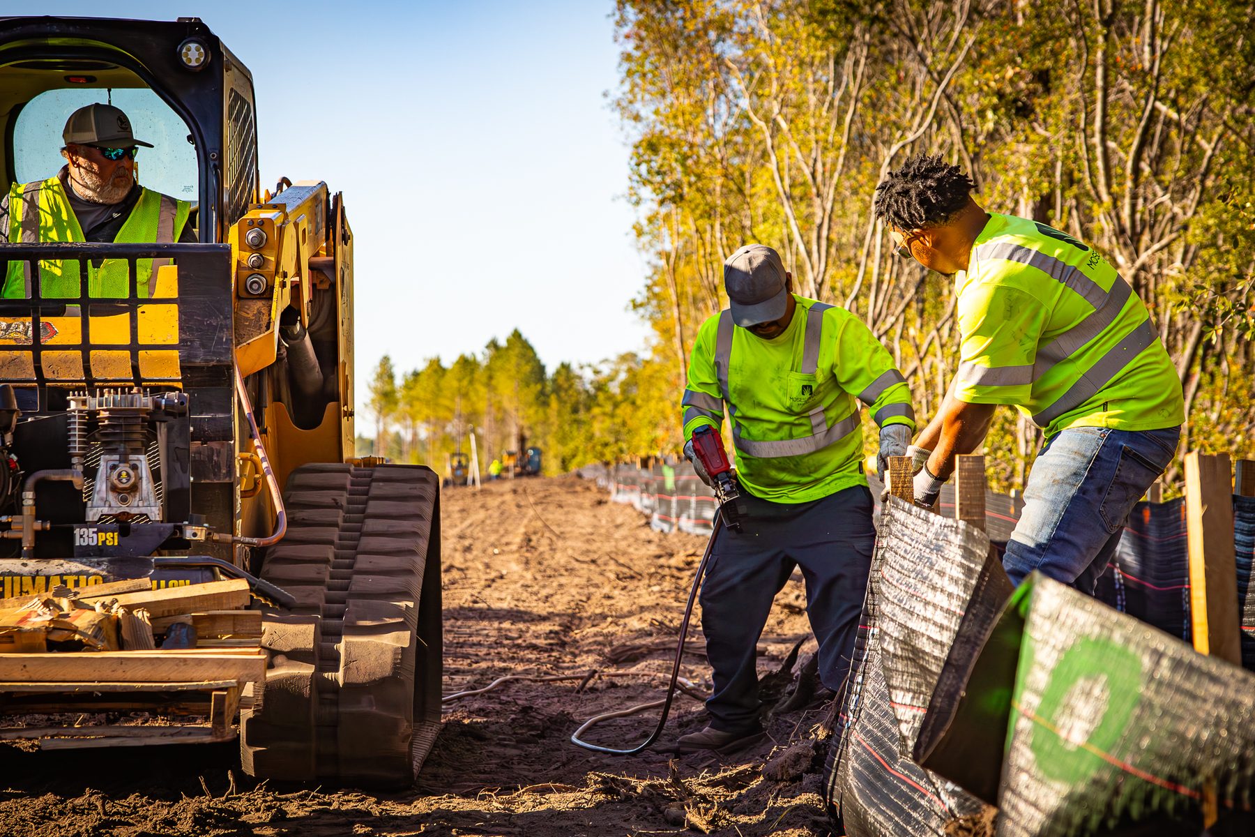 **Alt Text:** Crew members work on installing a silt fence for the industrial park expansion in Jesup, GA. One operator manages heavy machinery while colleagues prepare the erosion control barriers, ensuring the project runs smoothly and...