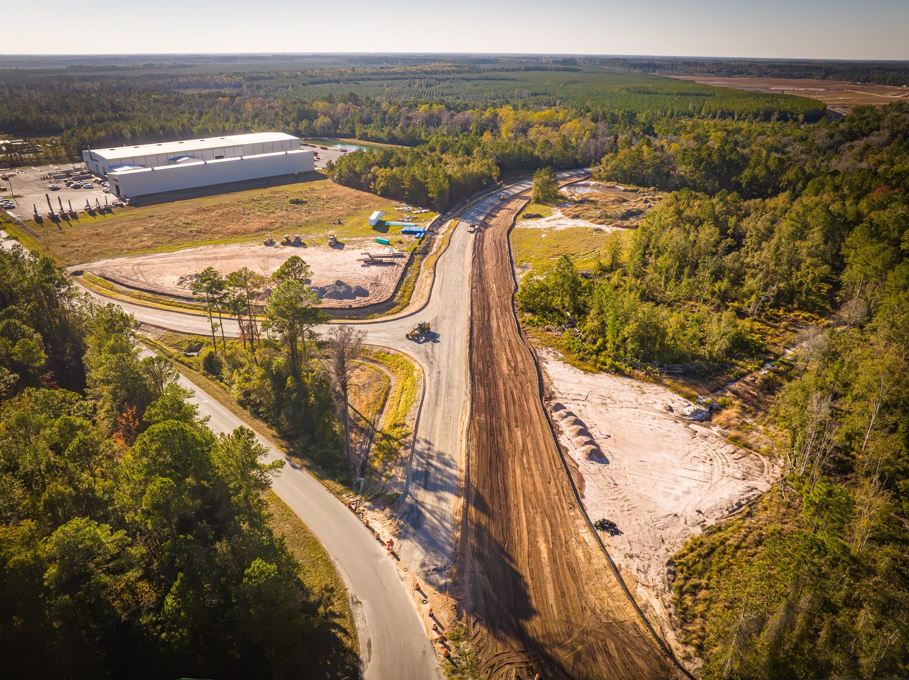 **Alt Text:** Aerial view of site preparation for an industrial park expansion in Jesup, GA. Heavy machinery is visible along newly graded roads, while a silt fence is installed to manage erosion, emphasizing Moses Grass Company's commit...