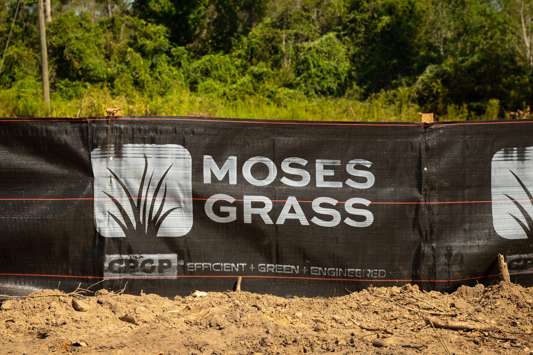 **Alt Text:** A section of a silt fence at a construction site on Hammond Church Rd in Lyons, GA, prominently displaying the Moses Grass Company logo. The banner highlights their focus on efficient, green, and engineered grass solutions ...