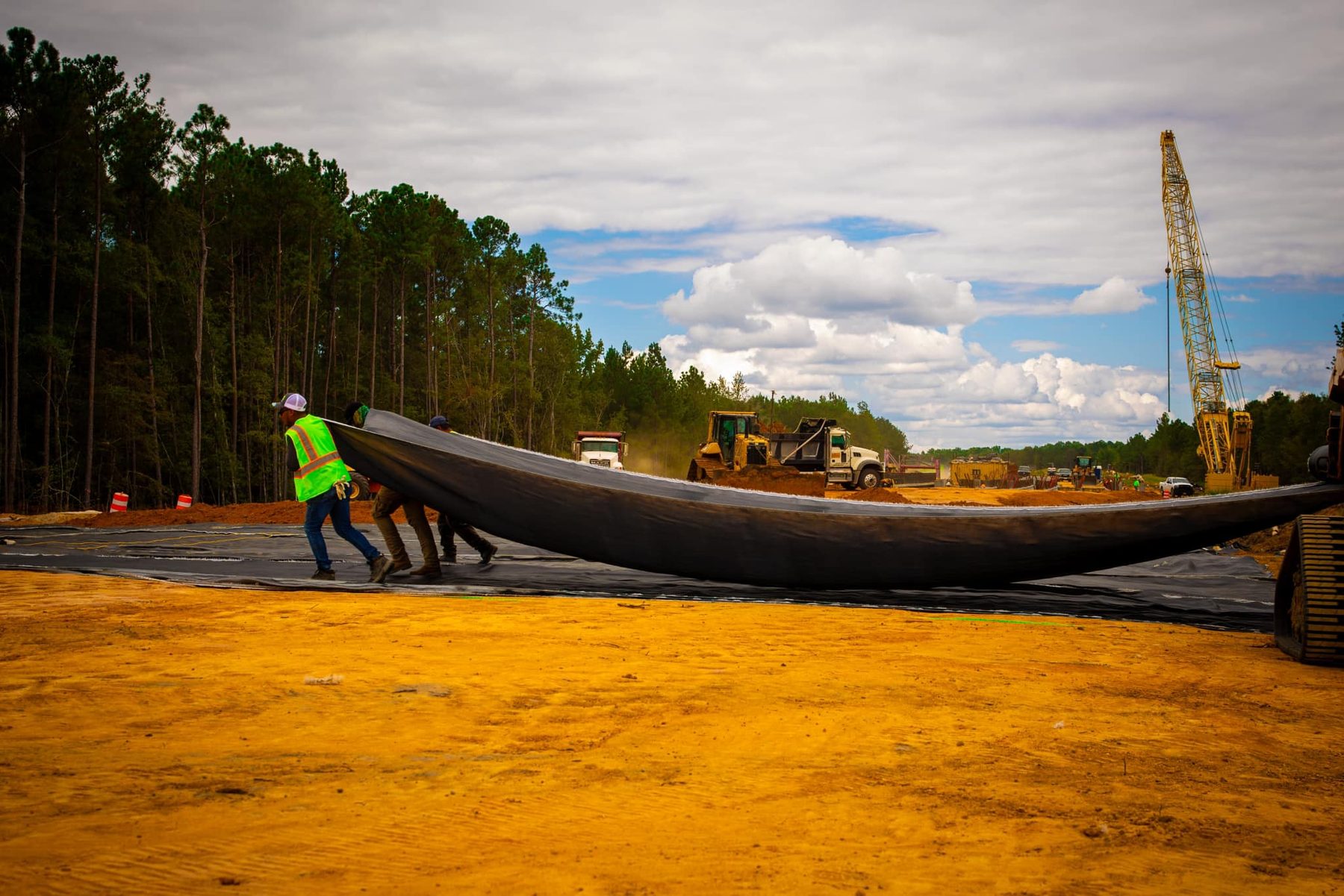 **Alt Text:** Crew members are laying down geotextile fabric for stabilization on the US 1 Bypass project in Toombs County, GA. This essential step helps ensure soil protection and erosion control on site.