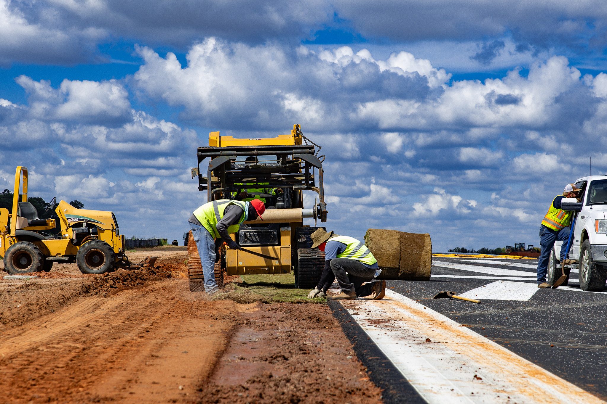 Crew installing sod along a pavement edge with skid steer support in Macon, GA.