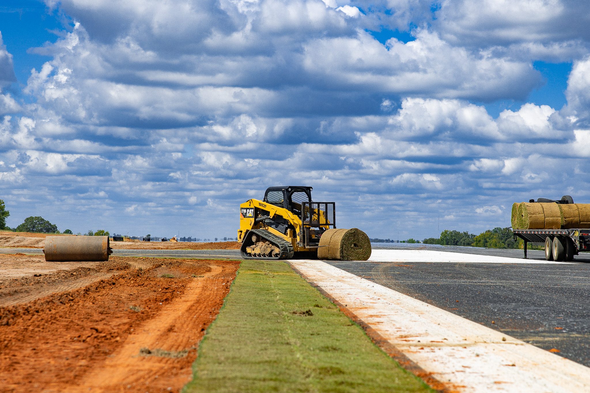 Skid steer moving a sod roll along the pavement edge in Macon, GA.
