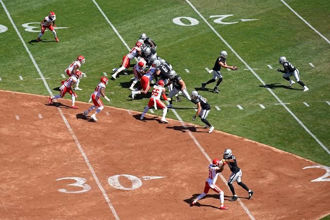 De Raiders gaan voor een rushing play en de quarterback staat op het punt de football aan zijn running back te geven in het Coliseum.