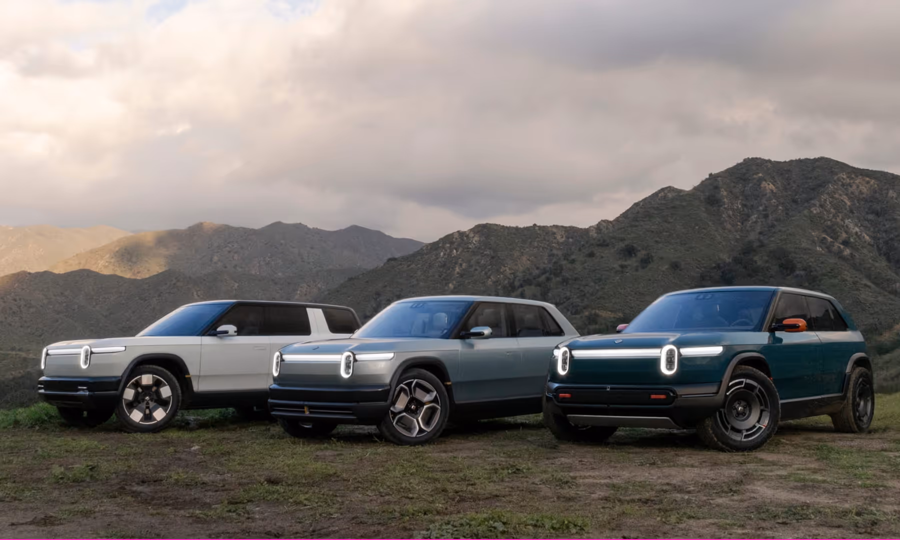 Three Rivian vehicles in front of mountains