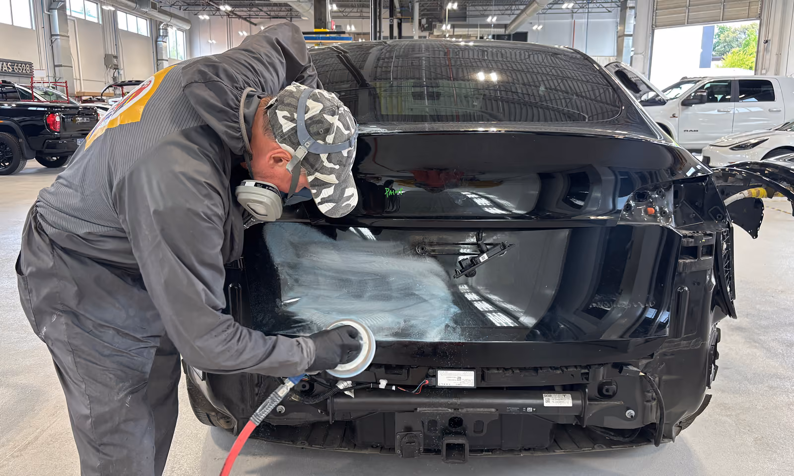 A technician professionally buffing a Tesla in an autobody shop.