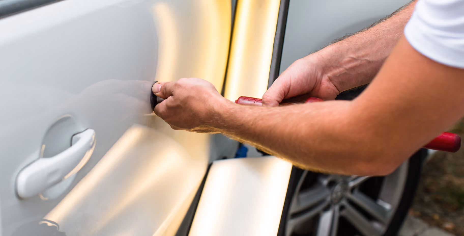 A technician using paintless dent repair technology to repair a white car