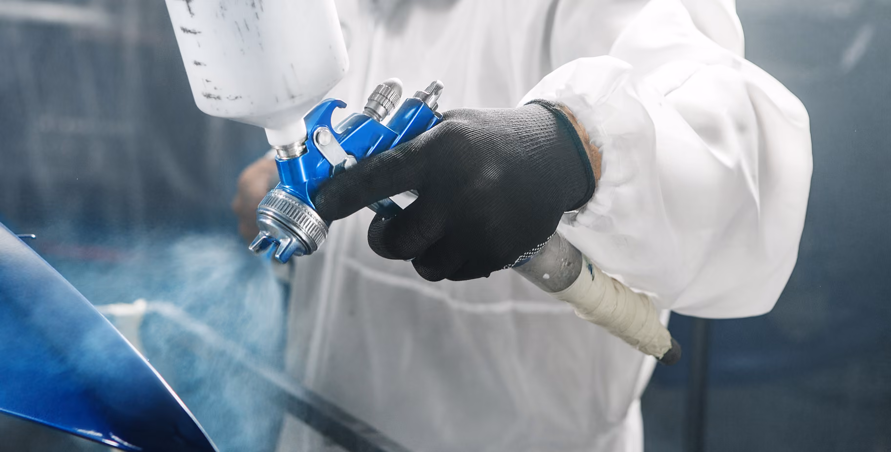 A professional technician spraying a paint gun, colour matching a blue car.