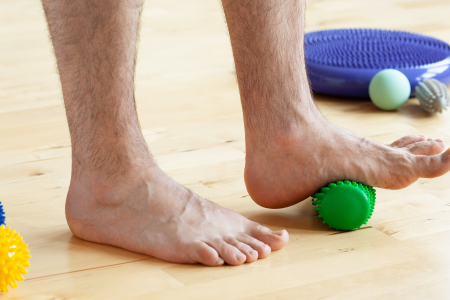 Close-up of a person using a green massage ball under their arch to relieve discomfort from flat feet during a physical therapy session.