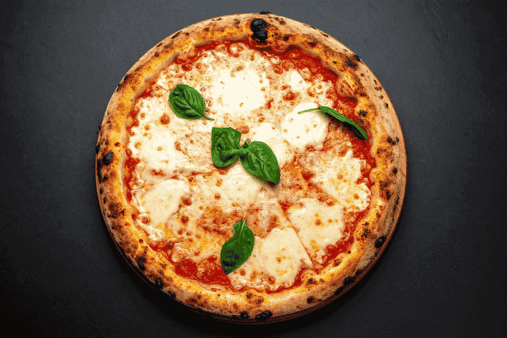 Pizza margherita cuite au four avec mozzarella fondante et feuilles de basilic – exemple de pizza réalisée lors d’une formation pizzaiolo en ligne.