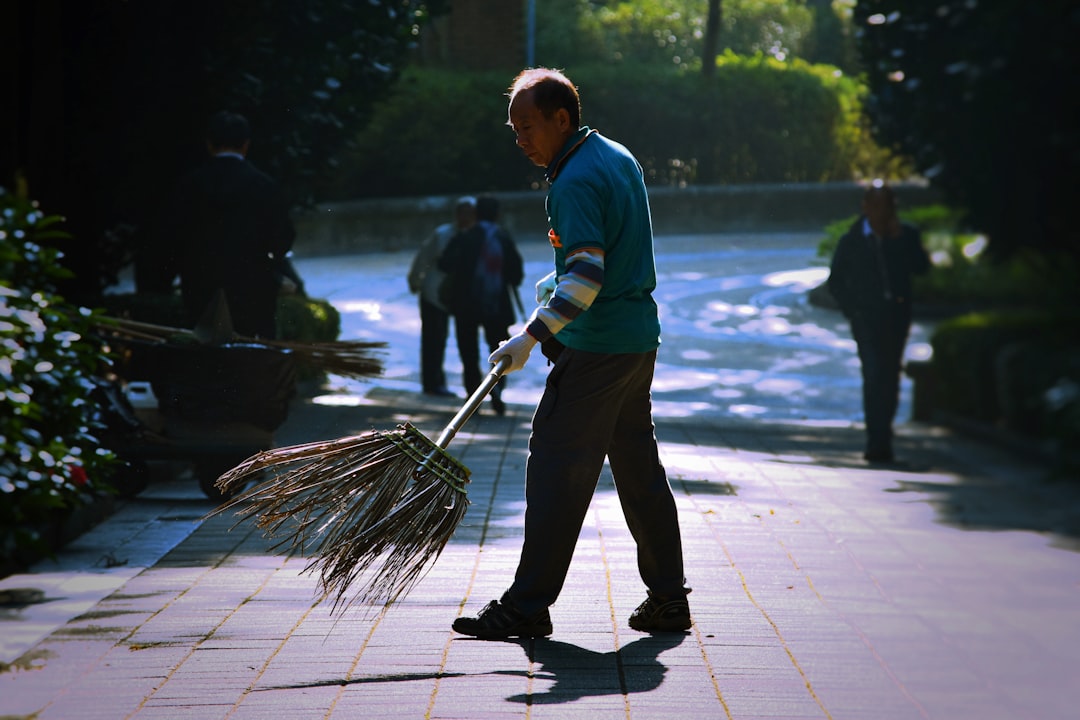 A person sweeping leaves and debris off a paver patio with a broom - paver patio maintenance A person sweeping leaves and debris off a paver patio with a broom - paver patio maintenance