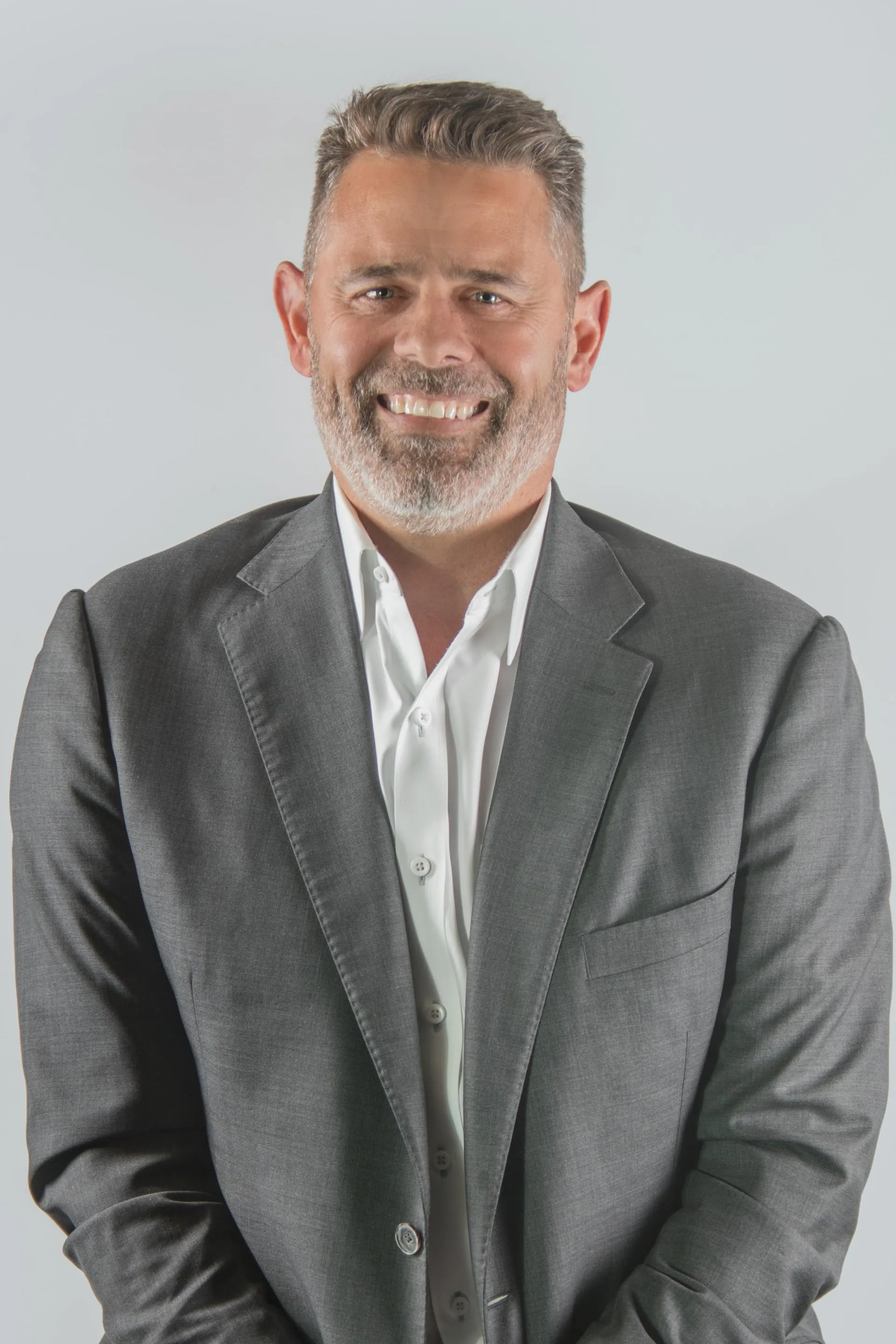 Professional headshot of Craig Jewett, Owner of Jewett Construction, wearing a dark grey suit and white shirt, smiling confidently. He leads the company with a vision for excellence in Single-Source Design-Build solutions.