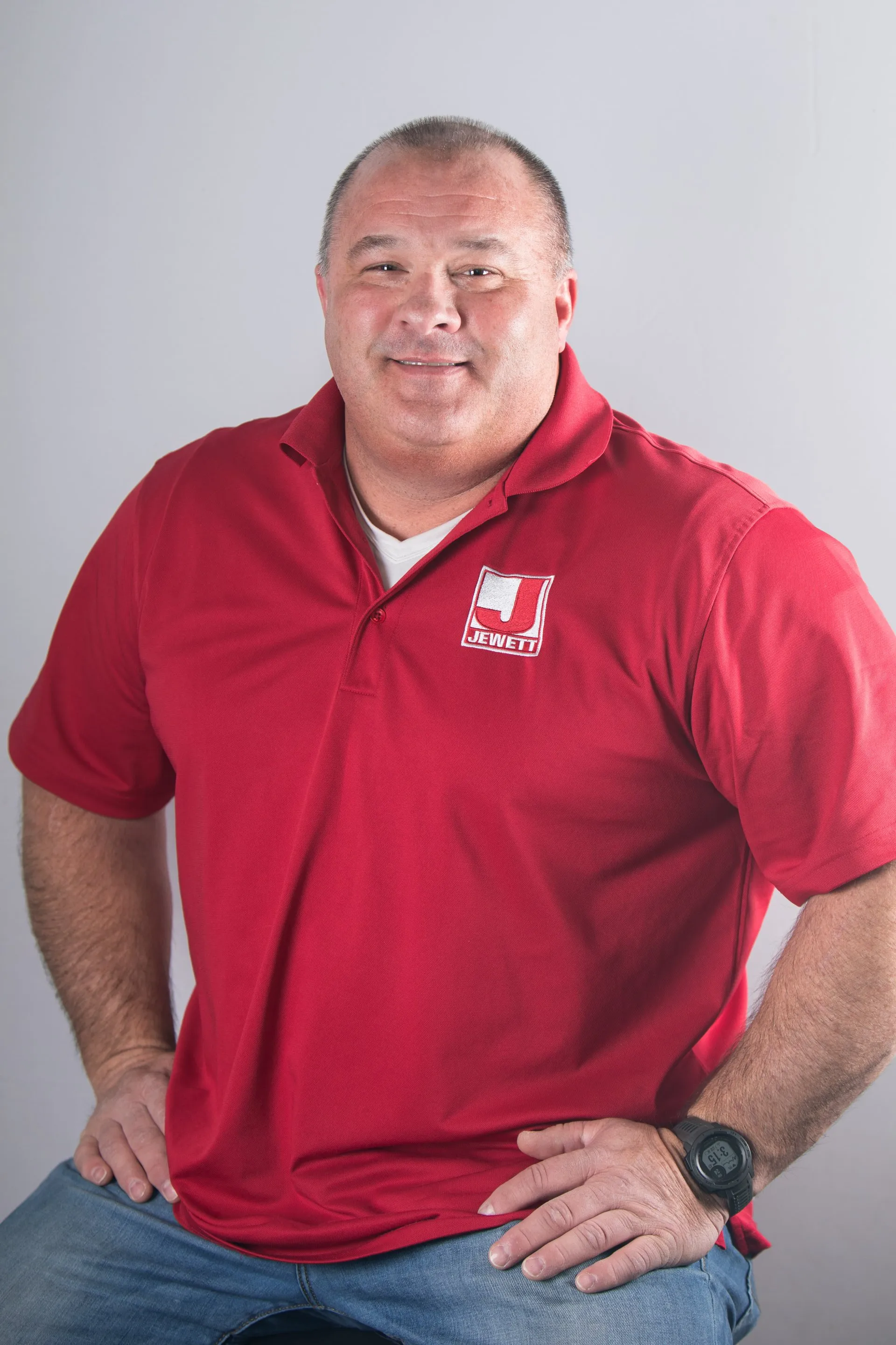 Headshot of Damon Brown, General Superintendent at Jewett Construction, wearing a red company polo and a black wristwatch, smiling. He brings over 30 years of industry experience and Marine Corps values to jobsite leadership.
