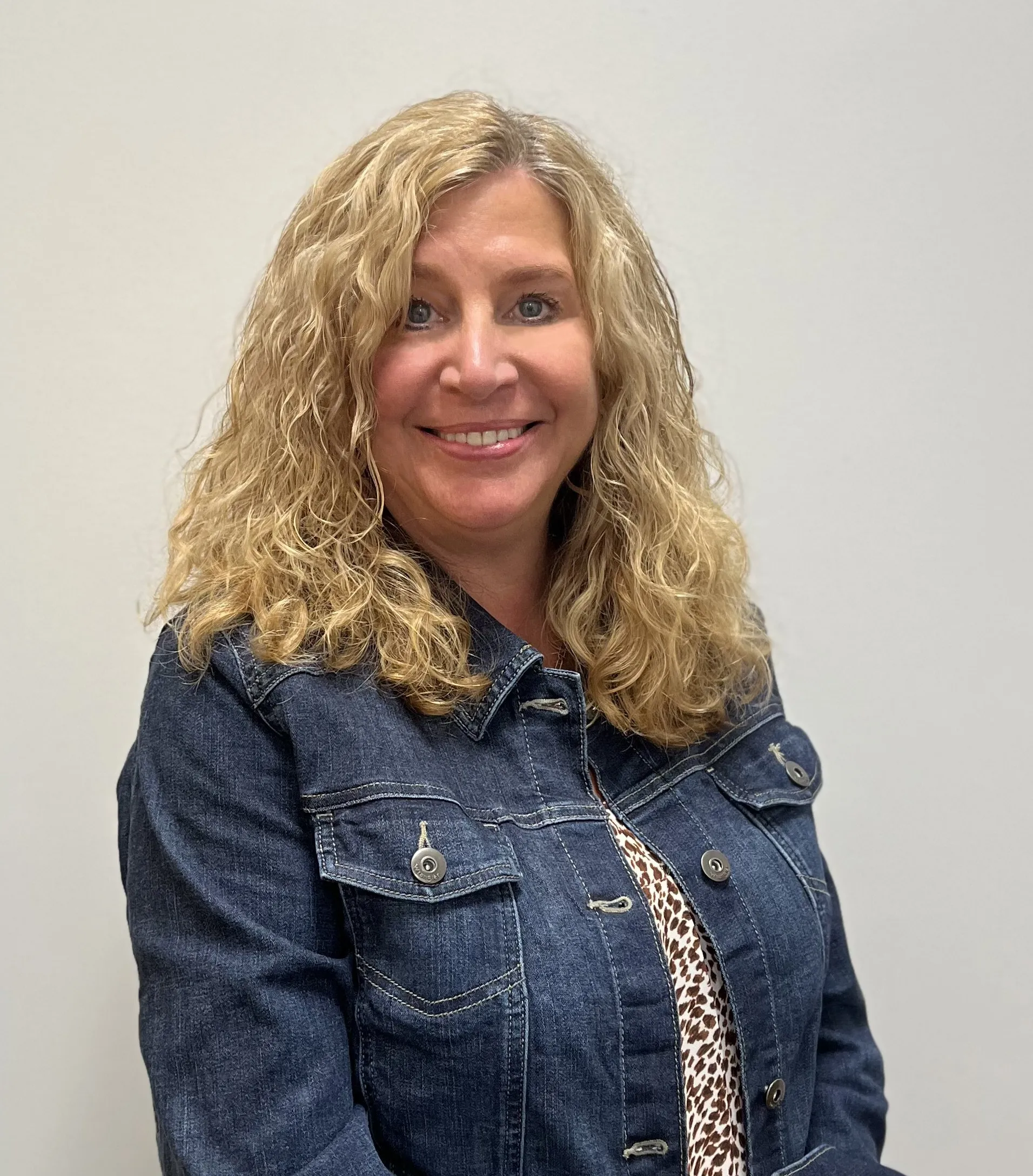 Headshot of Diane Grillo, Vice President of Finance at Jewett Construction, wearing a denim jacket and patterned blouse, smiling. She leads financial operations, ensuring efficiency and profitability.