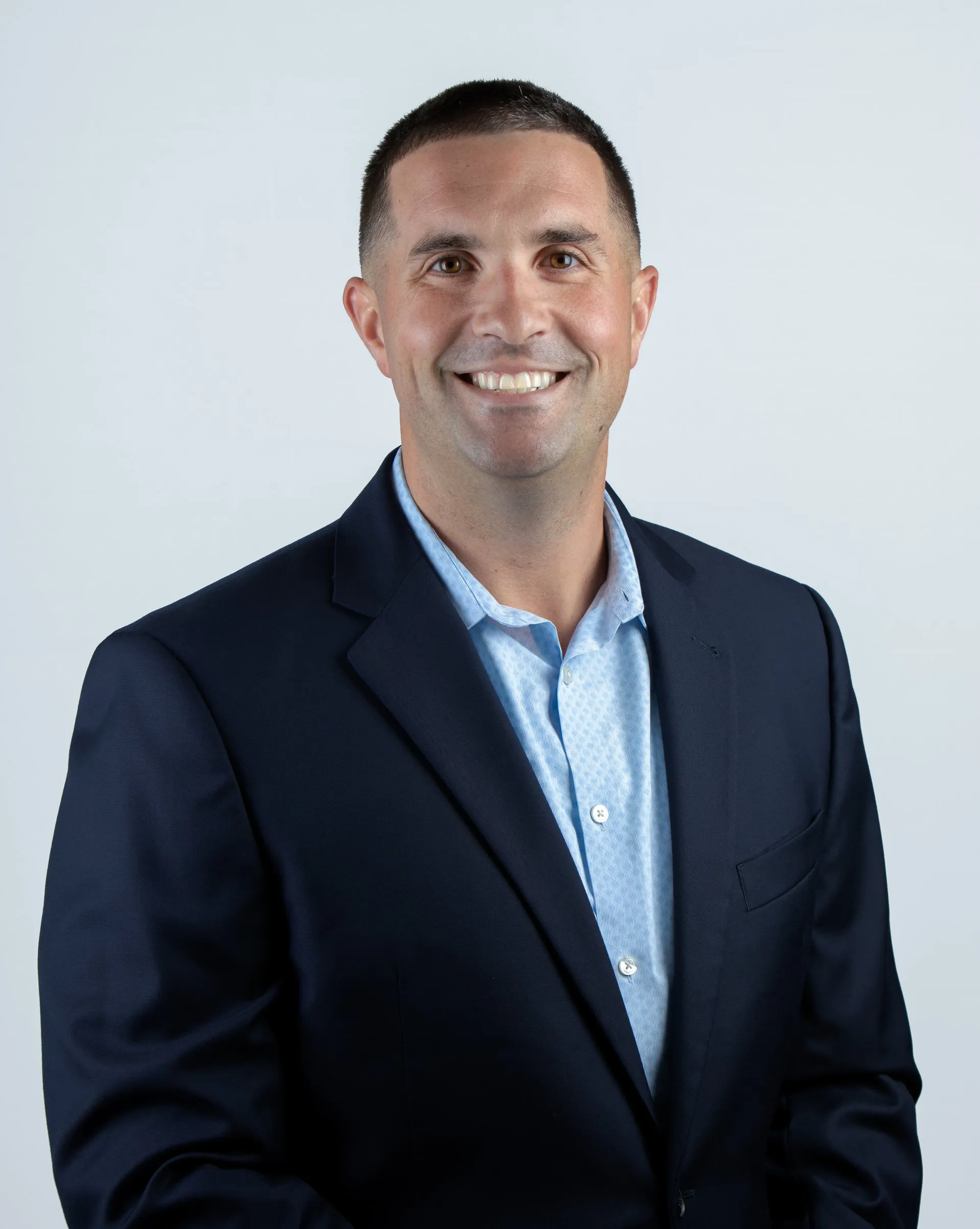 Professional headshot of Greg Stewart, President of Jewett Construction, wearing a navy suit and light blue dress shirt, smiling. He drives strategic growth and ensures operational excellence.
