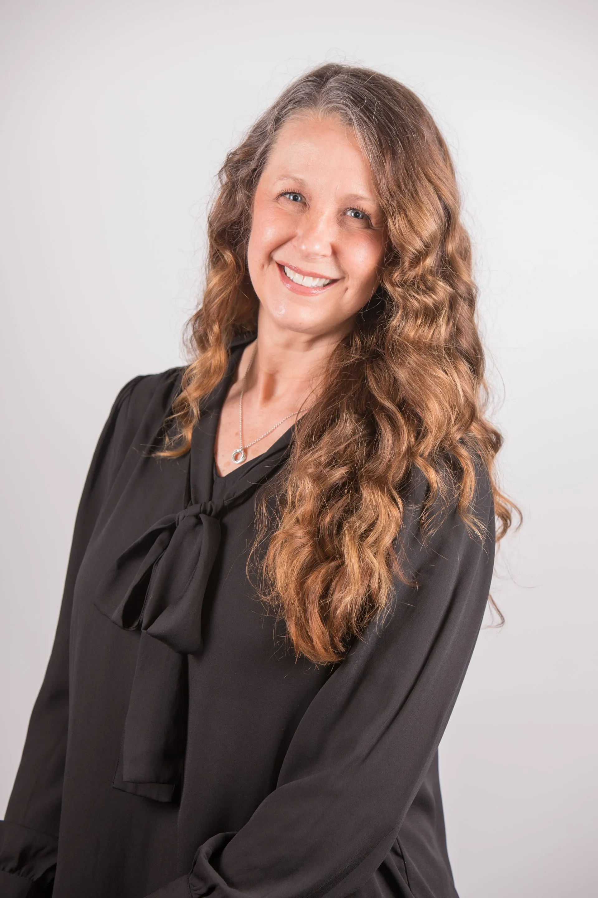 Headshot of Lynn Palmer, Director of Human Resources at Jewett Construction, wearing a black blouse with a bow and long, wavy hair, smiling. She fosters a thriving workplace culture and employee development.