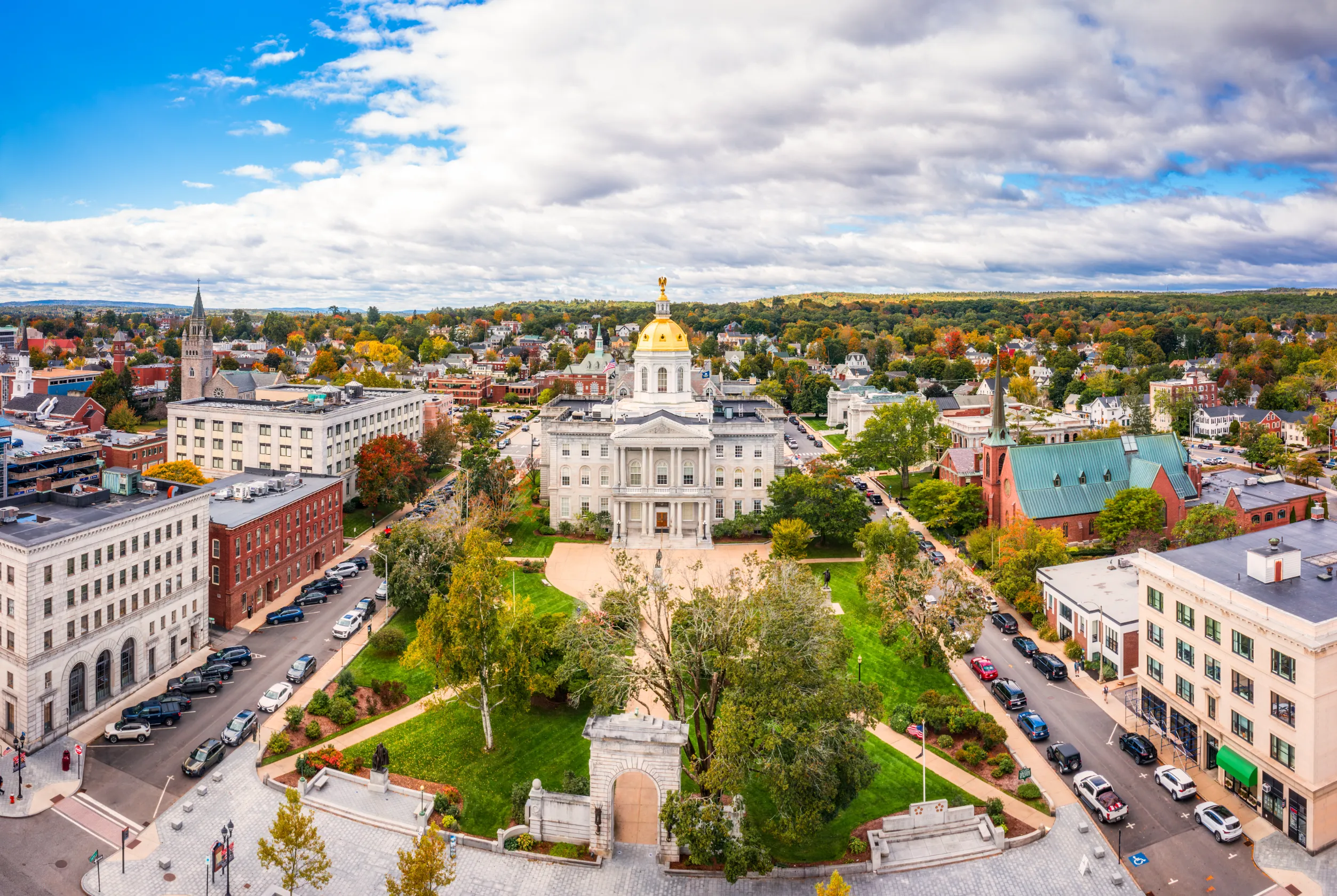 A picturesque aerial view of the New Hampshire State House in Concord, surrounded by historic buildings and colorful fall foliage.