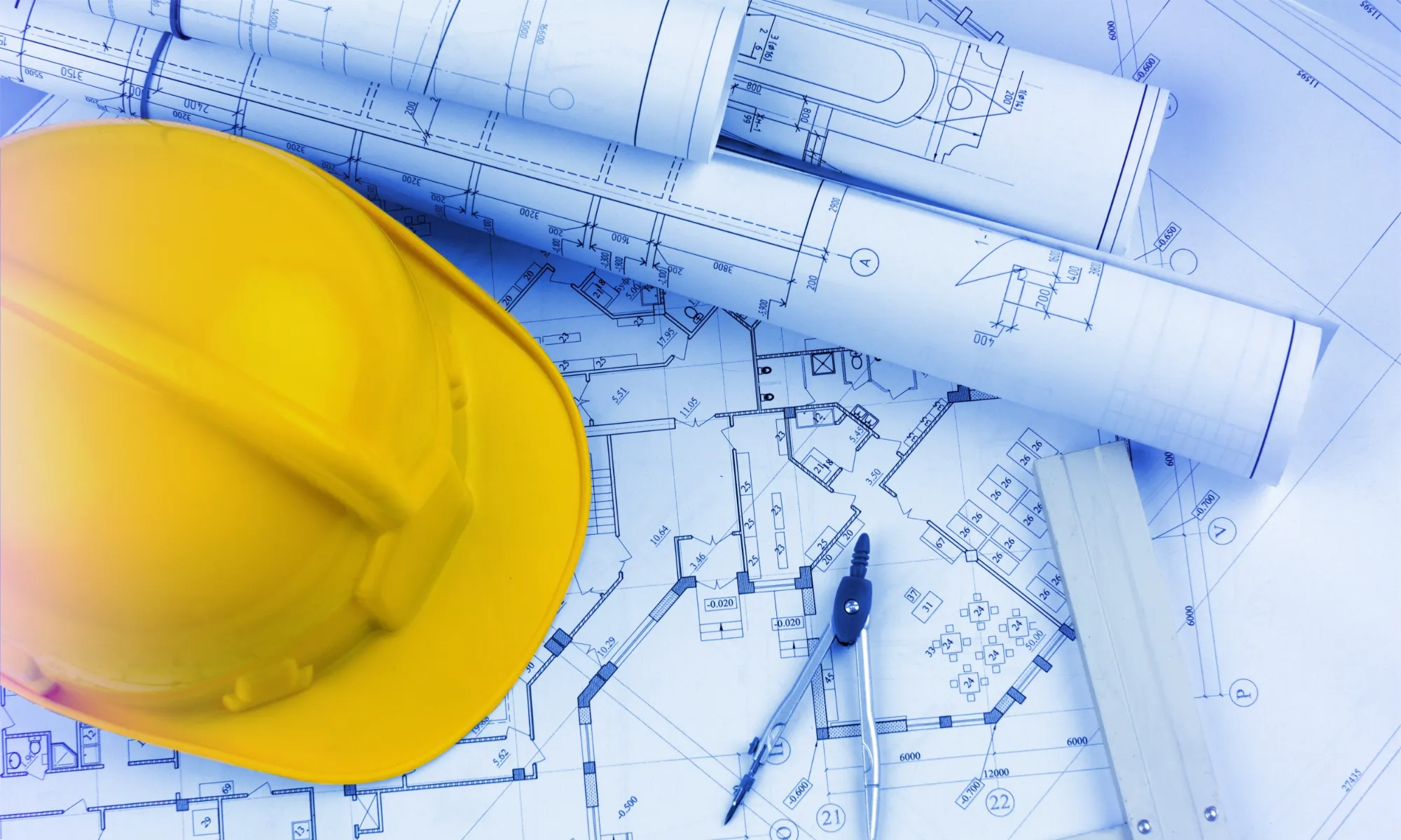 A close-up shot of architectural blueprints spread across a planning table, surrounded by construction tools and hard hats, emphasizing Jewett Construction’s integrated design-build approach that unifies planning and execution.